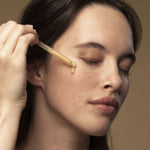 Woman applying a dropper of liquid to her face against a neutral background