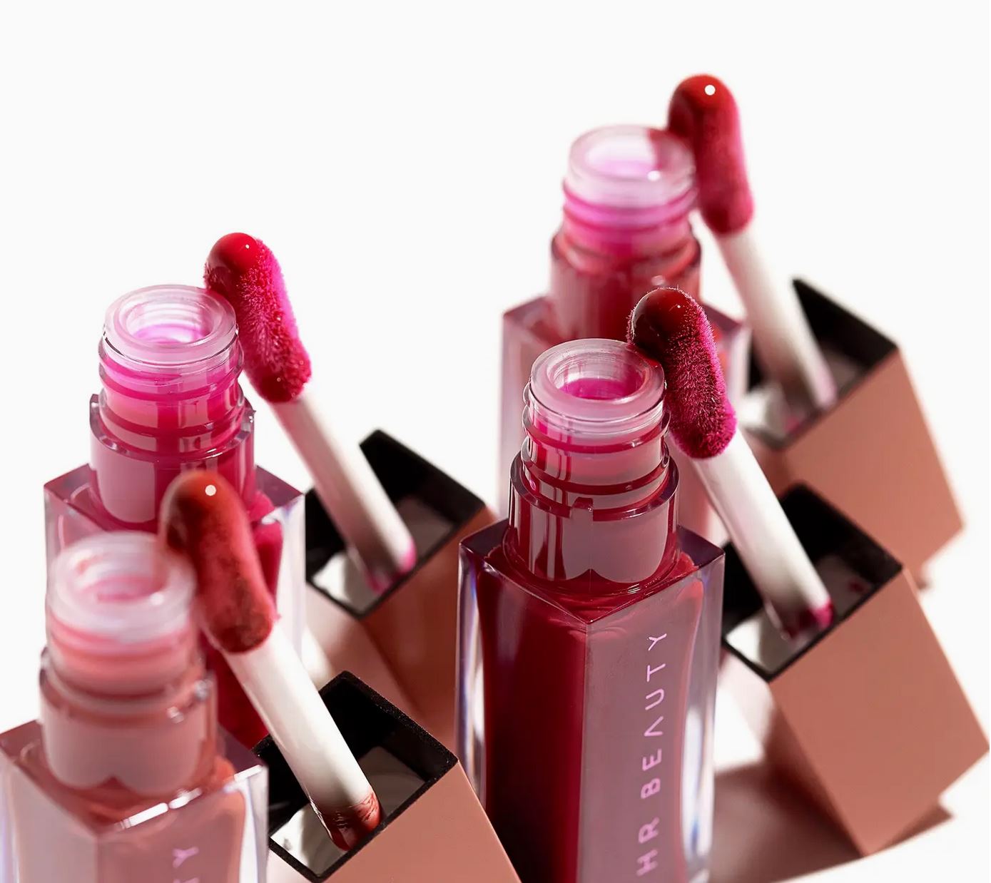 Set of pink lip glosses with applicators on a white background