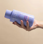 Hand holding a purple bottle of Epzen sensitive body wash with a beige background
