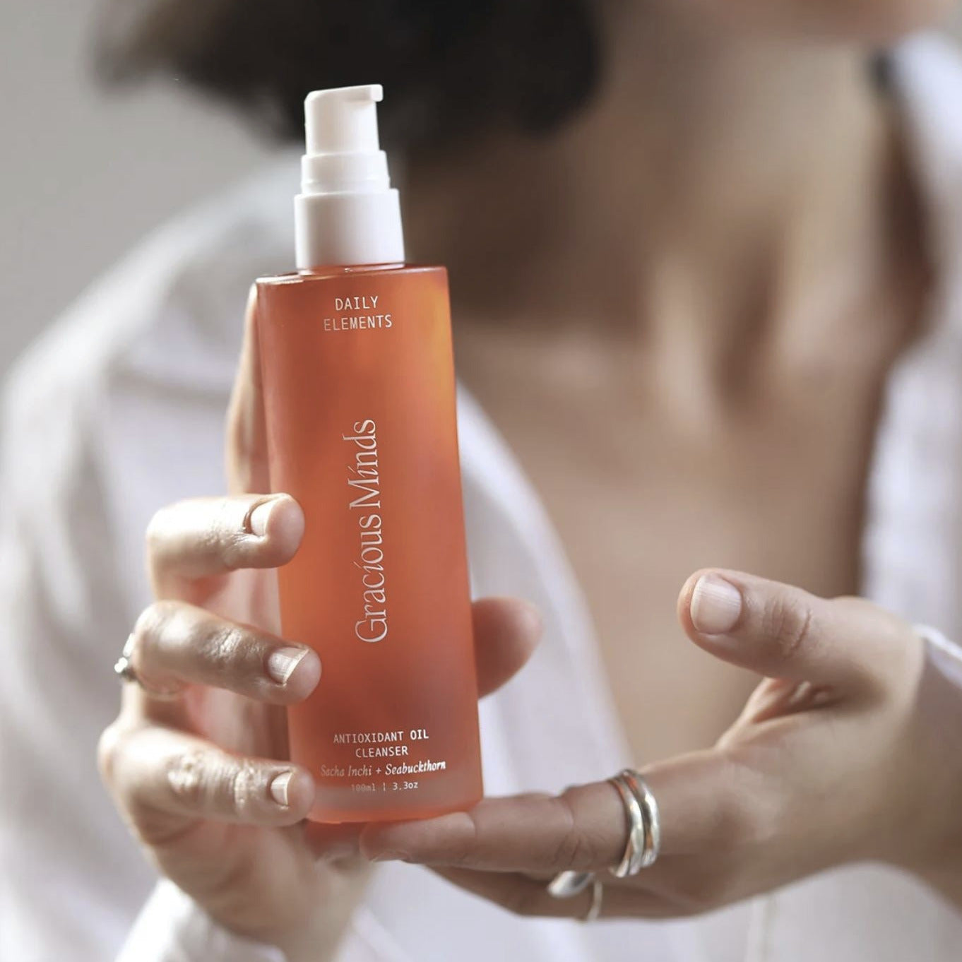 Person holding an orange bottle labeled 'Gracious Minds' with a blurred background
