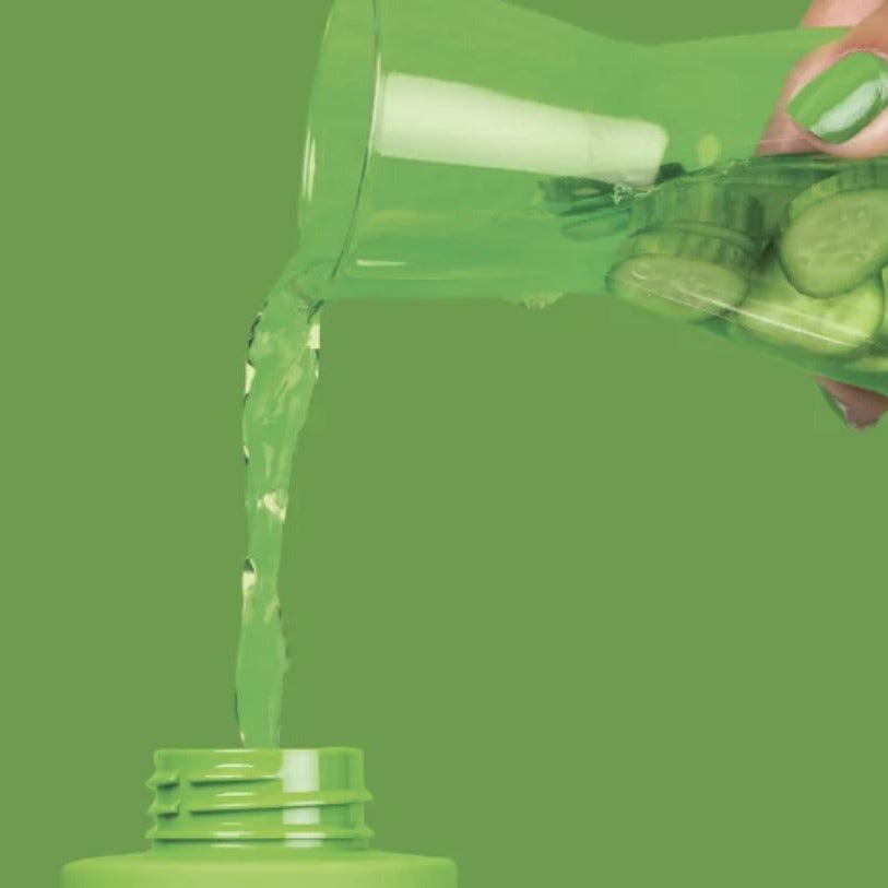 Green bottle being poured with cucumbers inside on a green background