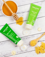 Two Weleda Skin Food tubes on a wooden surface with honey and wooden spoons.
